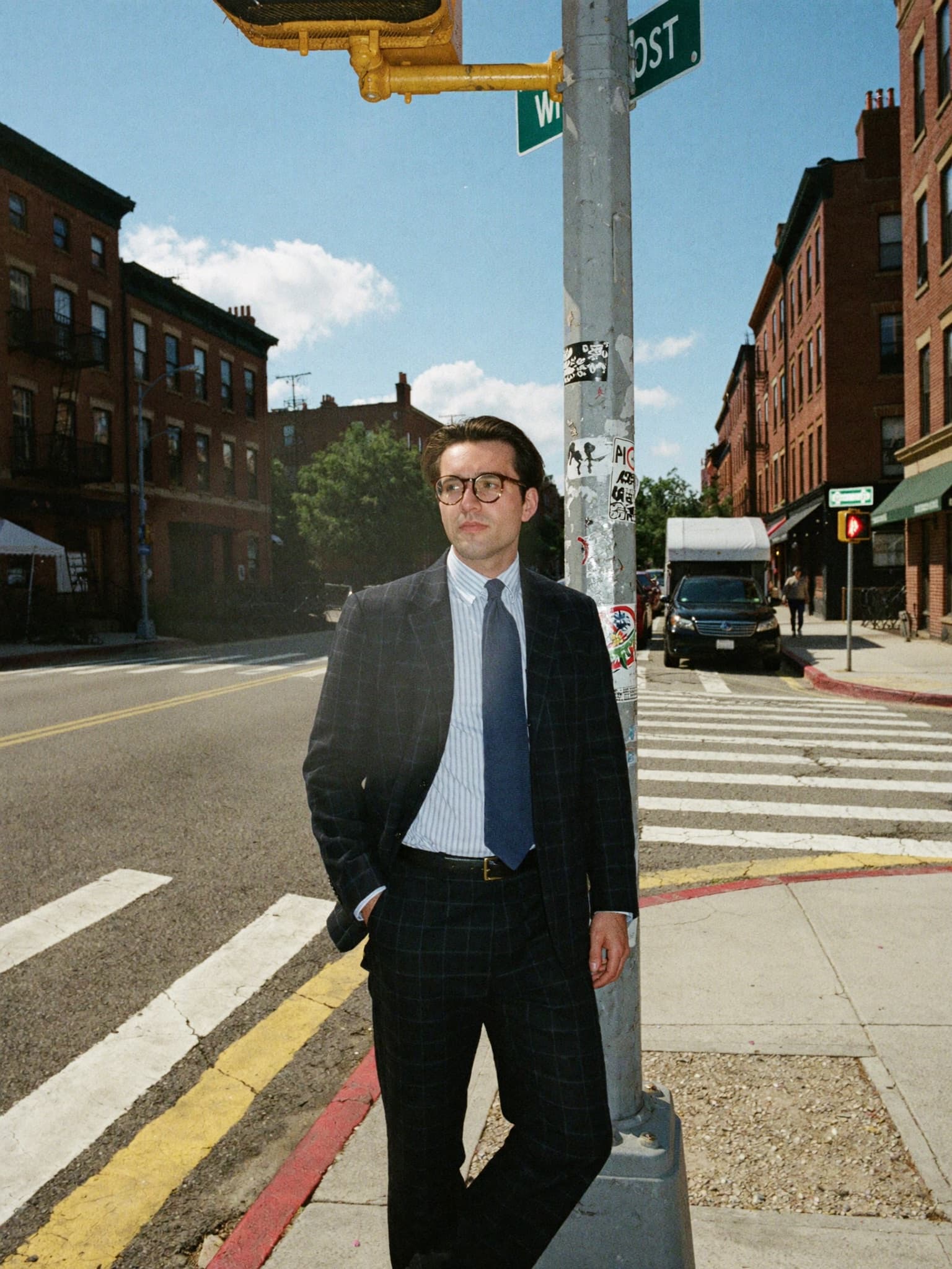 Zachary LaCorte in a navy suit and tie, leaning against a signal post on a Boston corner